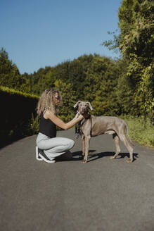 Woman stroking dog crouching on footpath - MTBF01273