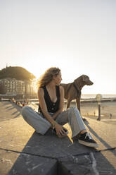 Young woman sitting with dog on promenade - MTBF01275