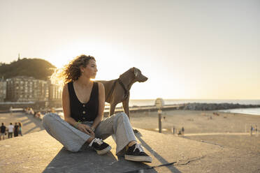 Woman spending leisure time with dog sitting on promenade - MTBF01276