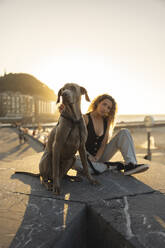 Young woman woman sitting with dog on promenade - MTBF01277