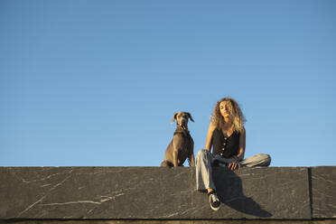 Junge Frau sitzt mit Hund an der Wand - MTBF01282