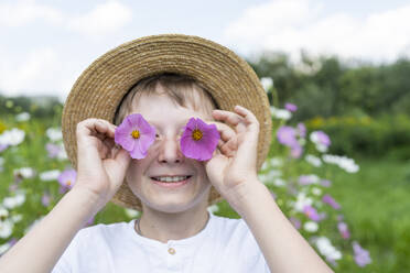 Glücklicher Junge hält rosa Blumen über die Augen im Garten - VBUF00357