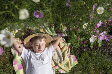 Lächelnder Junge mit Hut auf einer Decke im Garten liegend - VBUF00361