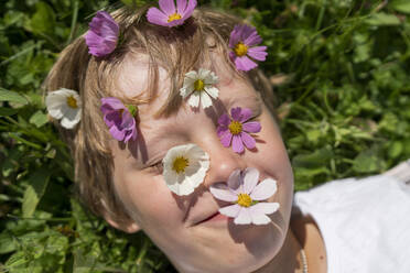 Lächelnder Junge mit Blumen über dem Gesicht an einem sonnigen Tag - VBUF00365