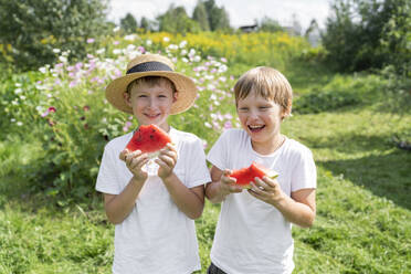 Glückliche Jungen mit Wassermelonenscheiben im Garten stehend - VBUF00367