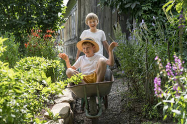 Smiling boy with brother sitting in wheelbarrow on sunny day - VBUF00370