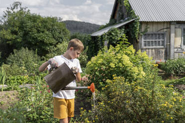 Junge gießt Blumen mit Gießkanne im Garten an einem sonnigen Tag - VBUF00373