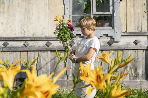 Boy with bouquet of flowers standing in front of wooden house - VBUF00386