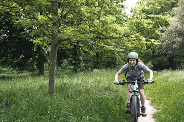 Glückliche Frau fährt Fahrrad inmitten eines Fahrrads im Wald - AMWF01666