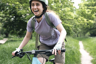 Happy woman enjoying riding bicycle in forest - AMWF01667