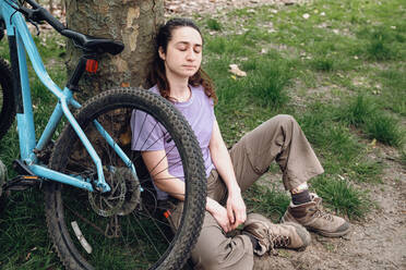 Junge Frau macht Pause in der Nähe von Fahrrad unter Baum im Wald - AMWF01668