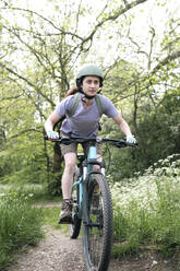 Woman wearing helmet riding bicycle in forest - AMWF01672