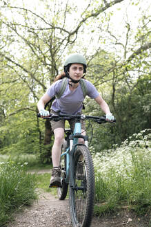 Frau mit Helm beim Fahrradfahren im Wald - AMWF01672