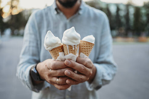 Man standing with melting ice cream cones - ANAF02020