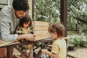 Father assisting sons in making wooden crate in back yard - ANAF02025