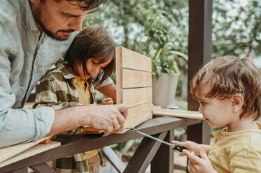 Father assisting son in using screwdriver for preparation of wooden crate - ANAF02026