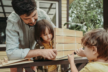 Father and sons preparing wooden crate in back yard - ANAF02027