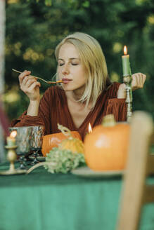 Blonde Frau mit geschlossenen Augen riecht Kürbissuppe am Esstisch - VSNF01366