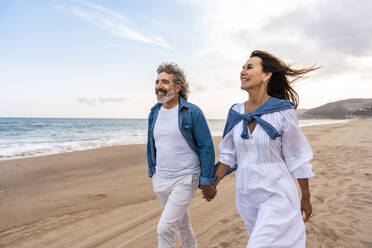 Happy senior couple holding hands walking at beach - OIPF03389