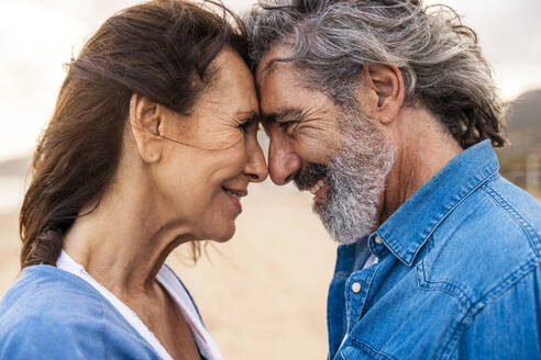Lächelndes älteres Paar, das sich am Strand die Stirne berührt - OIPF03399
