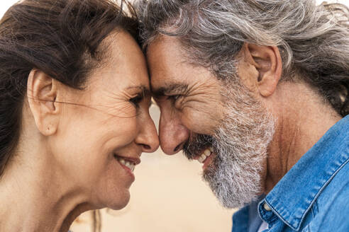 Glückliches älteres Paar, das sich am Strand an der Stirn berührt - OIPF03400