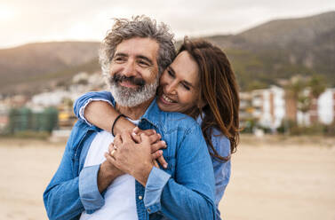 Happy senior woman embracing man from behind at beach - OIPF03412