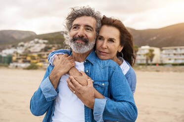 Senior woman hugging man from behind at beach - OIPF03414