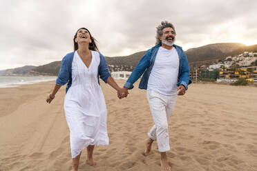 Cheerful couple holding hands and walking on sand - OIPF03419