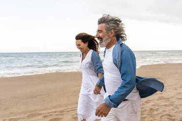 Happy senior couple enjoy walking on sand by sea - OIPF03420