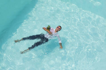 Happy man swimming with pineapple in pool - VRAF00134