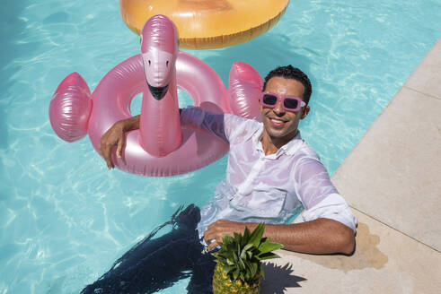 Glücklicher Mann mit aufblasbarem Schwimmring im Pool an einem sonnigen Tag - VRAF00135