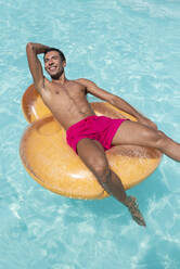 Happy young man sitting on inflatable float in pool - VRAF00137