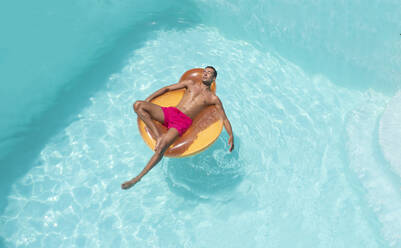 Junger Mann entspannt sich auf einem aufblasbaren Schwimmer im Pool - VRAF00138