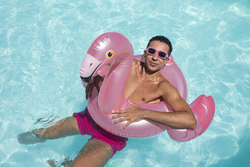 Lächelnder Mann schwimmt mit aufblasbarem Ring im Pool - VRAF00144