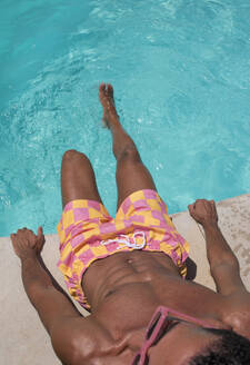 Junger Mann sitzt am Pool an einem sonnigen Tag - VRAF00149