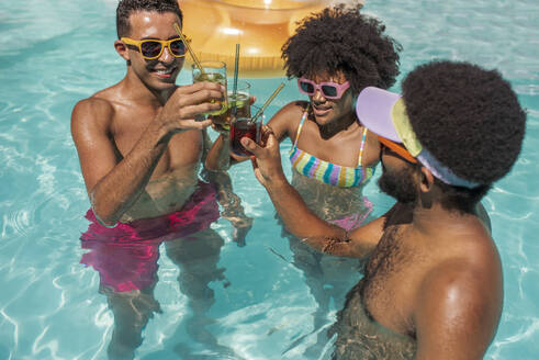 Freunde stoßen gemeinsam mit Getränken im Pool an einem sonnigen Tag an - VRAF00168