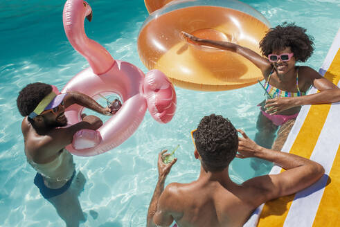 Glückliche Freunde mit aufblasbaren Schwimmern, die sich im Pool vergnügen - VRAF00175