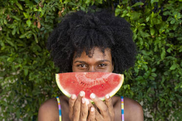 Junge Frau mit Wassermelonenscheibe vor Pflanzen - VRAF00181