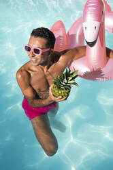 Lächelnder Mann mit Ananas schwimmt im Pool - VRAF00192