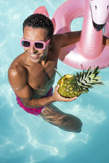 Glücklicher Mann hält Ananas und schwimmt im Wasser - VRAF00193