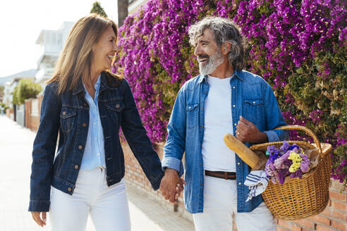 Glücklicher älterer Mann mit Picknickkorb, der die Hand einer Frau hält - OIPF03443