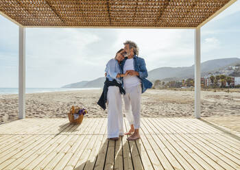 Glückliches älteres Paar, das sich am Wochenende in einem Pavillon am Strand umarmt - OIPF03456