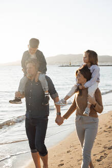 Eltern, die ihre Kinder auf den Schultern tragen und am Strand spazieren gehen - JOSEF20620