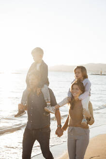 Eltern, die ihre Kinder auf den Schultern tragen und am Strand spazieren gehen - JOSEF20622