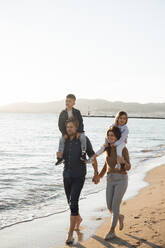 Parents carrying children on shoulders and walking by sea on sunny day - JOSEF20623