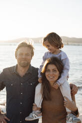 Smiling man and woman with daughter in front of sea - JOSEF20628