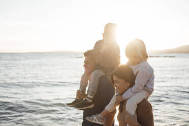 Kinder sitzen auf den Schultern der Eltern am Meer am Strand - JOSEF20632