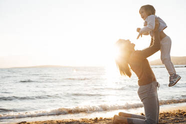 Happy mother lifting daughter up in air at beach - JOSEF20645