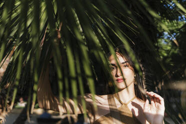 Junge Frau zwischen Palmenblättern an einem sonnigen Tag - PBTF00209