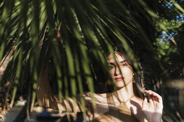 Young woman between palm leaves on sunny day - PBTF00209